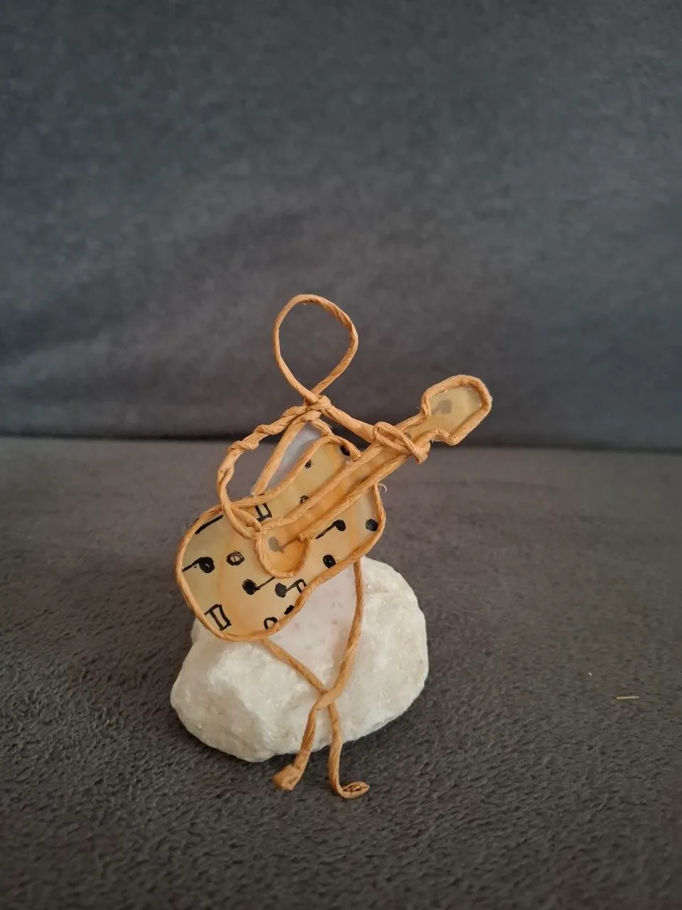 Nahaufnahme einer Papierdraht-Figur mit selbst bemaltem Gitarren-Motiv auf einem kleinen Steinsockel