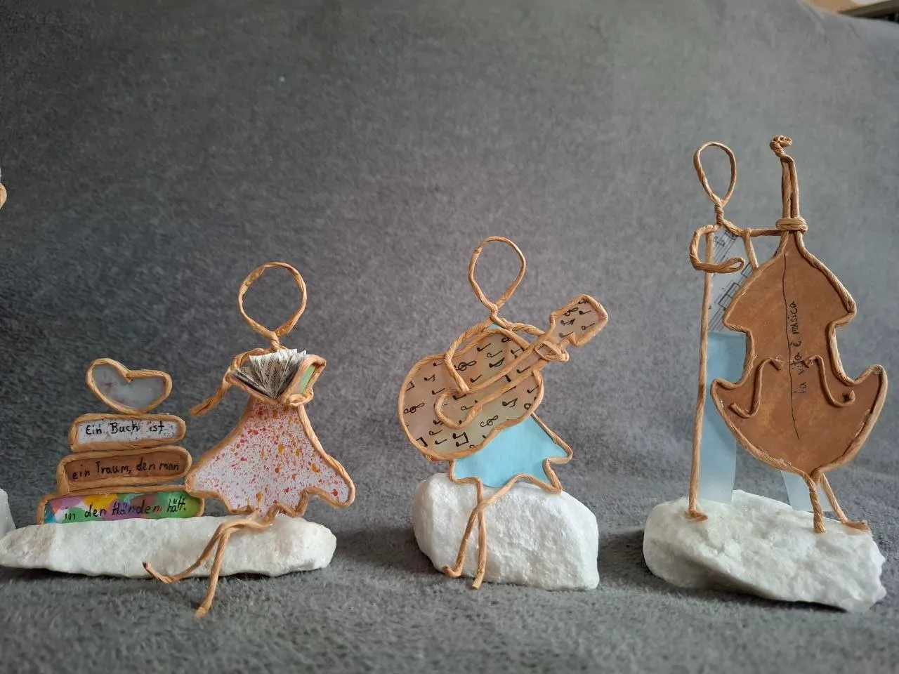 Drei Papierdraht-Figuren: eine mit Buch, eine mit Gitarre und eine mit Kontrabass, jeweils mit passendem Motiv